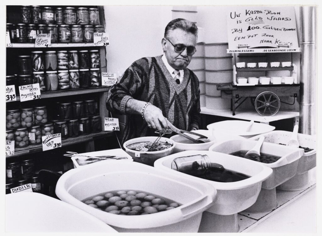 Mr. de Leeuw in the sour store 'De Leeuw' circa. 1989. In the back a sale advertisement which says: 'Your receipt is worth money. A 100 receipt is a jar of sour of your choosing'.